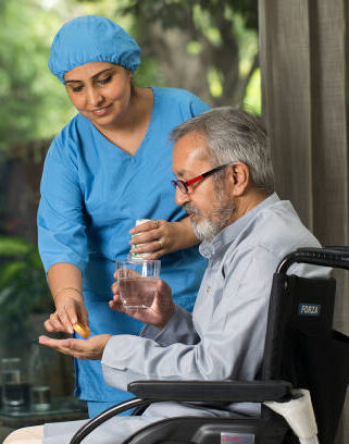 Female nurse giving medicine to disabled old man on wheelchair